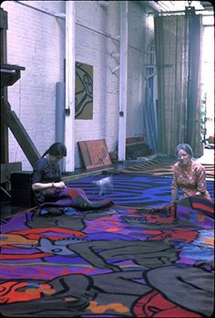 two people are sitting on the floor in an art gallery looking at their paintings and rugs