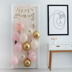 balloons are hanging on the wall in front of a happy birthday sign and framed artwork