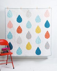 a quilted wall hanging next to a red chair in front of a white wall