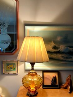 a lamp sitting on top of a wooden table next to a mirror and framed pictures