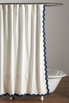 a white shower curtain with blue scalloped edges on a wooden floor next to a bathtub