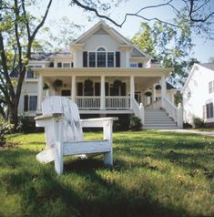 a white wooden bench sitting in front of a large house on a green grass covered field