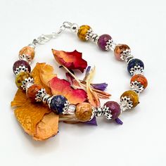 a bracelet with multicolored beads and leaves on it's end, sitting on a white surface