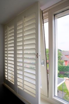 an open window with white shutters in front of it and a view of the outside