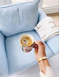 a person holding a cup of coffee in front of a blue chair with pillows on it