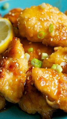 chicken wings with sauce and green onions on a blue plate next to lemon wedges