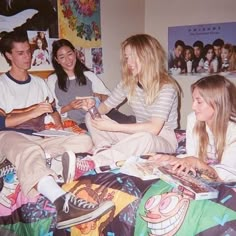 four people sitting on a bed with one woman looking at her phone and the other smiling