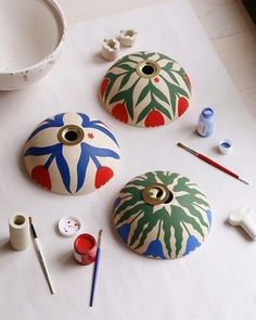 three painted pots sitting on top of a table next to paintbrushes and paints