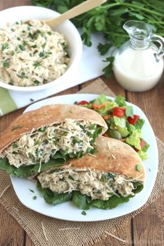 two white plates topped with sandwiches next to a bowl of salad