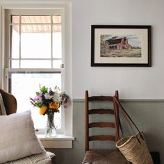 a chair and vase with flowers in front of a window on the wall next to a bench