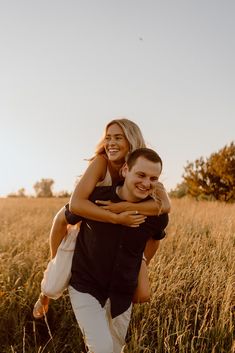 a man carrying a woman on his back in the middle of a field with tall grass