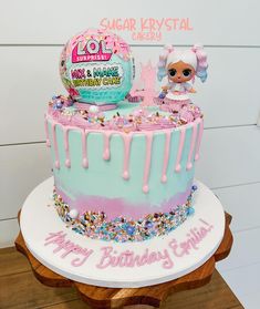 a pink and blue birthday cake with lol surprisers on top, sitting on a wooden stand