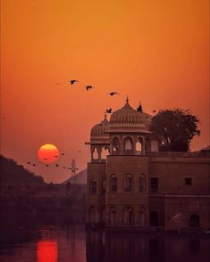 the sun is setting over an old building with birds flying in the air above it