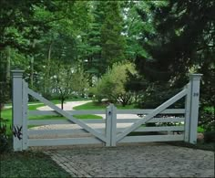 a white gate is open in the middle of a driveway with grass and trees around it