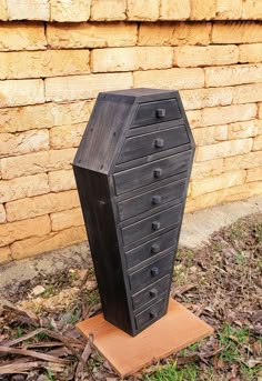 a tall black chest of drawers sitting on top of a wooden stand next to a brick wall