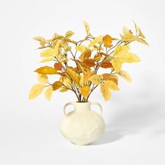 a white vase with yellow leaves in it