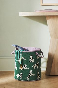 a green bucket with dogs on it sitting in front of a wooden table and chair