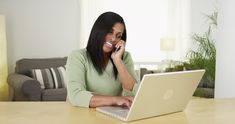 a woman sitting in front of a laptop computer talking on a cell phone and smiling