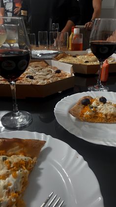 two slices of pizza sitting on top of white plates next to glasses of red wine