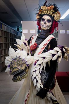 a woman in costume with flowers on her head and skeleton face paint holding a mask