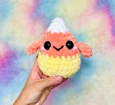 a hand holding a small stuffed animal in front of a colorful background with the shape of a sheep's head