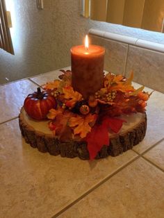 a candle that is sitting on top of a tree stump with leaves and pumpkins