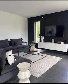 a living room with black walls and white furniture in the center, along with a large flat screen tv mounted to the wall