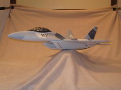 a model jet fighter plane sitting on top of a white cloth covered table next to a wall