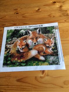 a cross stitch picture of three foxes on a wooden table