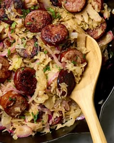 a skillet filled with sausages and sauerkraut next to a wooden spoon