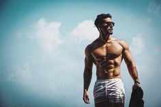 a shirtless man with no shirt on standing in the sand looking at the sky