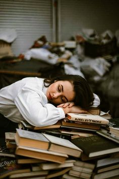 a woman laying on top of a pile of books next to a pile of other books