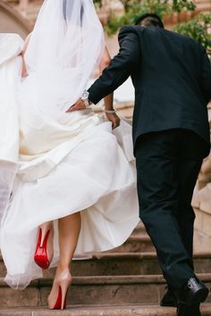 a bride and groom walking down the steps together with red shoes on their feet,