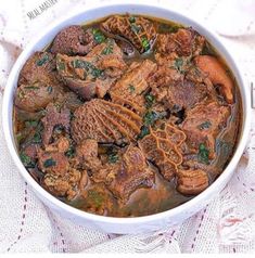 a bowl filled with meat and vegetables on top of a white table cloth next to a napkin