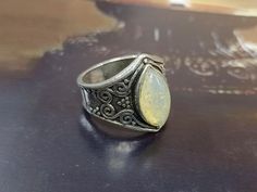 a silver ring with a yellow stone in it sitting on a table next to a vase