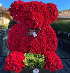 a large teddy bear made out of red roses sitting on the back of a truck