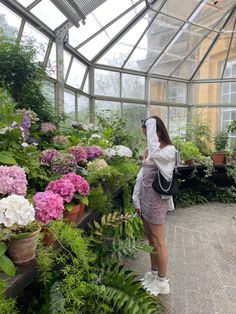 a woman is looking at flowers in a greenhouse