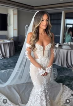 a woman in a wedding dress standing next to a bed with a veil on it