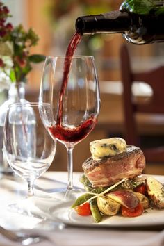 wine being poured from a bottle into a glass on a plate with vegetables and meat