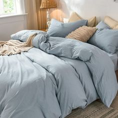 a bed with blue comforter and pillows in a bedroom next to a lamp on a table