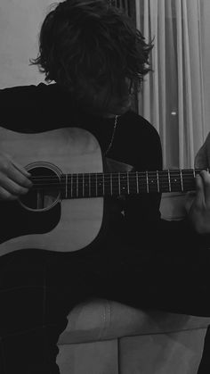 a person sitting on a couch playing an acoustic guitar