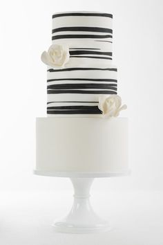 a three tiered cake with black and white striped frosting, flowers on top