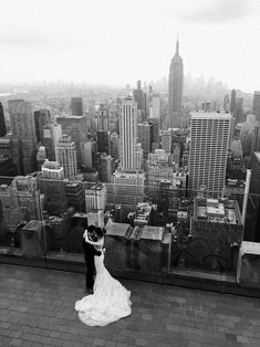 a bride and groom standing on top of a building in new york city, looking at the skyline