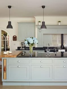 a kitchen with blue cabinets and flowers in the vase on the center island is surrounded by two black pendant lights