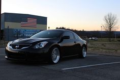 a black car parked in a parking lot next to an american flag on the building