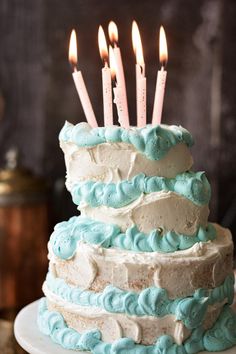 a blue and white cake with lit candles on it's top is sitting on a plate