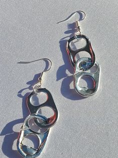 two pairs of silver earrings sitting on top of a white cloth covered surface, with one pair dangling from the back