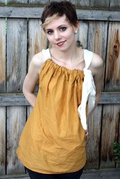 a woman standing in front of a wooden fence wearing an orange top and white shirt