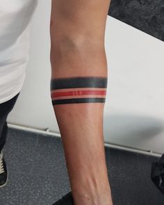 a person with a black and red striped tattoo on their arm, standing next to a white wall