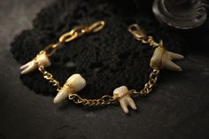 a gold chain bracelet with skulls and bones attached to the clasp, on a black background